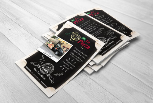 Una pila di menu di ristoranti su una superficie di legno presenta "La Pizza" con una grafica in stile lavagna, che ricorda un elegante biglietto da visita che Alghero potrebbe offrire. Ogni menu include una piccola foto di un forno per pizza, testo stilizzato e svolazzi decorativi con accenti verdi e rossi su uno sfondo bianco e nero. Volantini promozionali personalizzati stampati da PegPoint